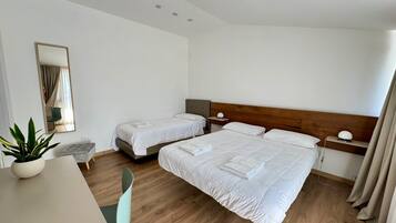 A hotel room with two beds, a desk, a chair, a potted plant, and a mirror.