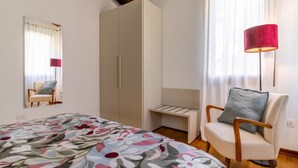 Een slaapkamer met een bed, een stoel, een kledingkast, een nachtkastje en een lamp.