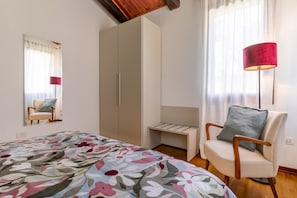 Ein Schlafzimmer mit einem Bett, einem Sessel, einem Kleiderschrank, einem Nachttisch und einer Lampe.