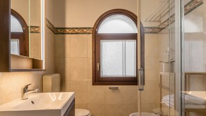 Een badkamer met een wastafel, toilet en bidet, met een houten opbergmeubel en een glazen douchecabine.
