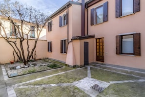 Ein Gebäude mit mehreren Fenstern, einer Tür und einem kleinen Garten mit Baum und Kies.