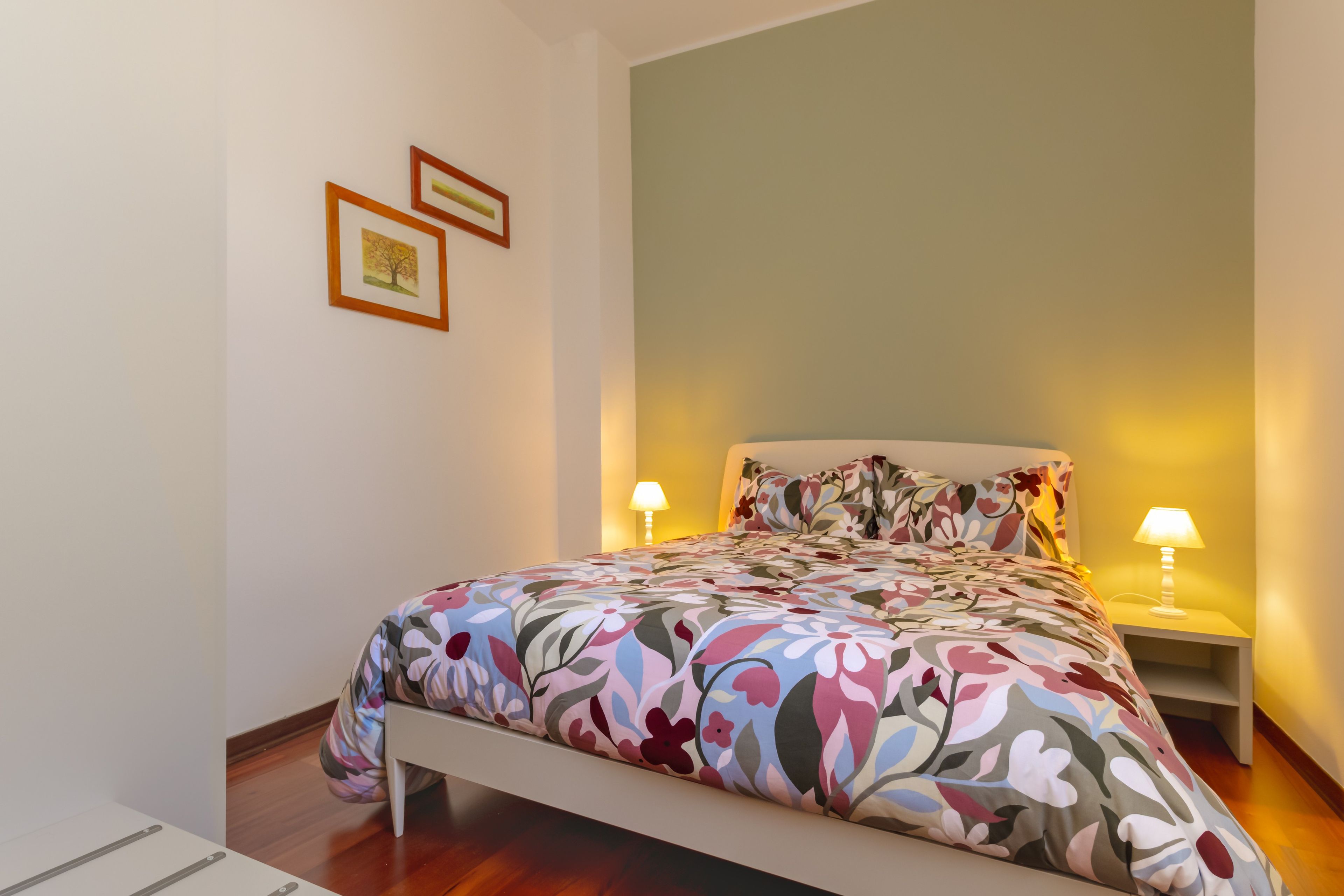 Ein Schlafzimmer mit einem Bett, zwei Nachttischlampen, einem Nachttisch und zwei gerahmten Bildern an der Wand.