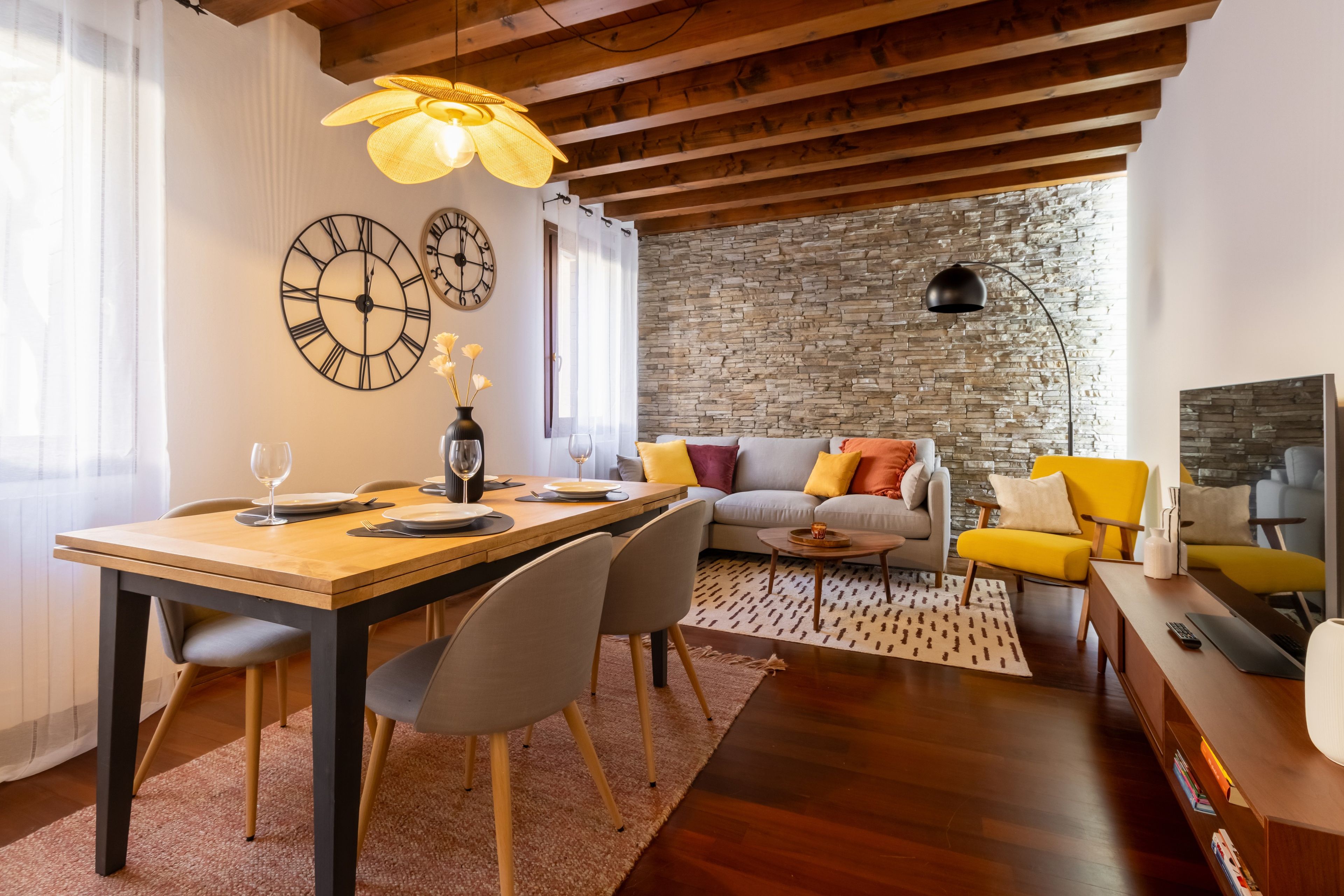 Un salon moderne avec un mur en pierre, un plafond en bois et un coin repas comprenant une table et des chaises en bois.