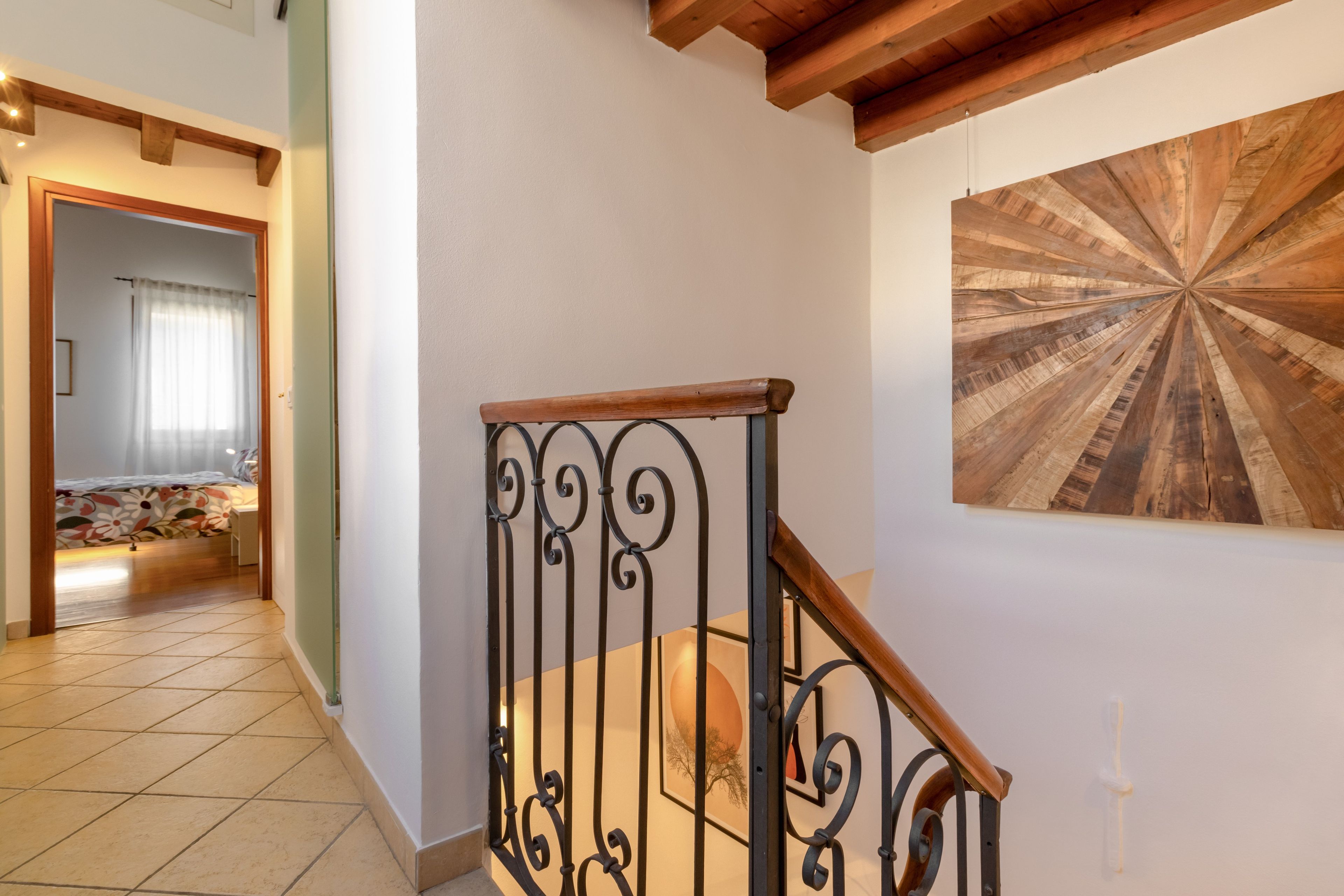 A staircase with a wooden handrail and black metal balusters, leading to a room with a large wooden floor design on the wall.