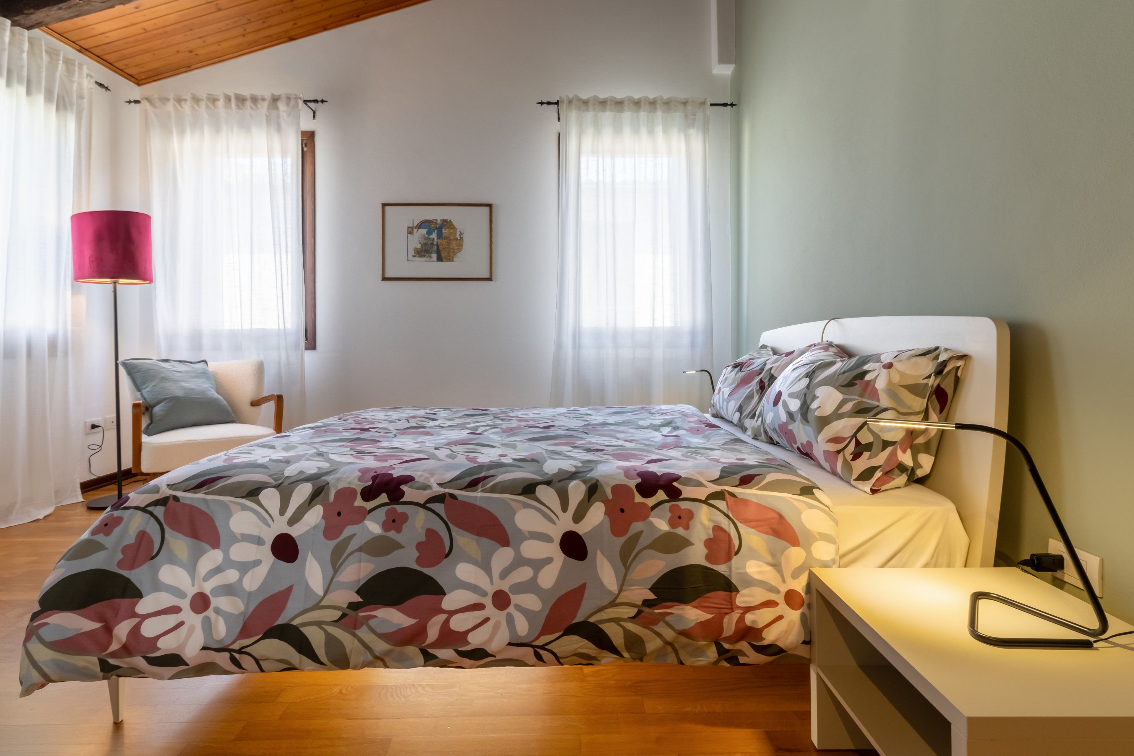 Une chambre à coucher avec un lit, une chaise, une table de chevet, une lampe et un tableau au mur.