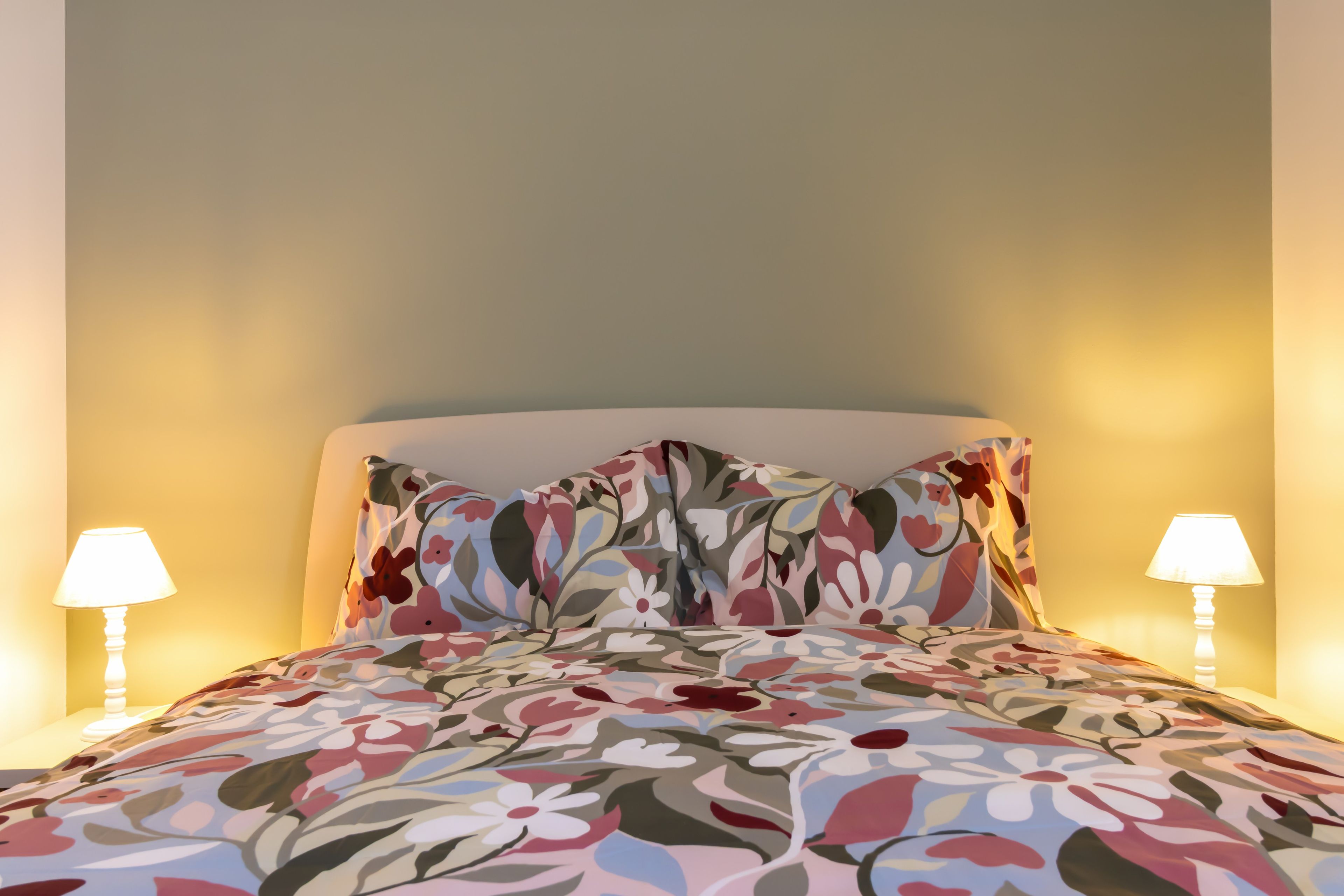 Ein Bett mit einem blumigen Bettüberwurf, zwei Nachttischlampen und eine schlichte Wand.