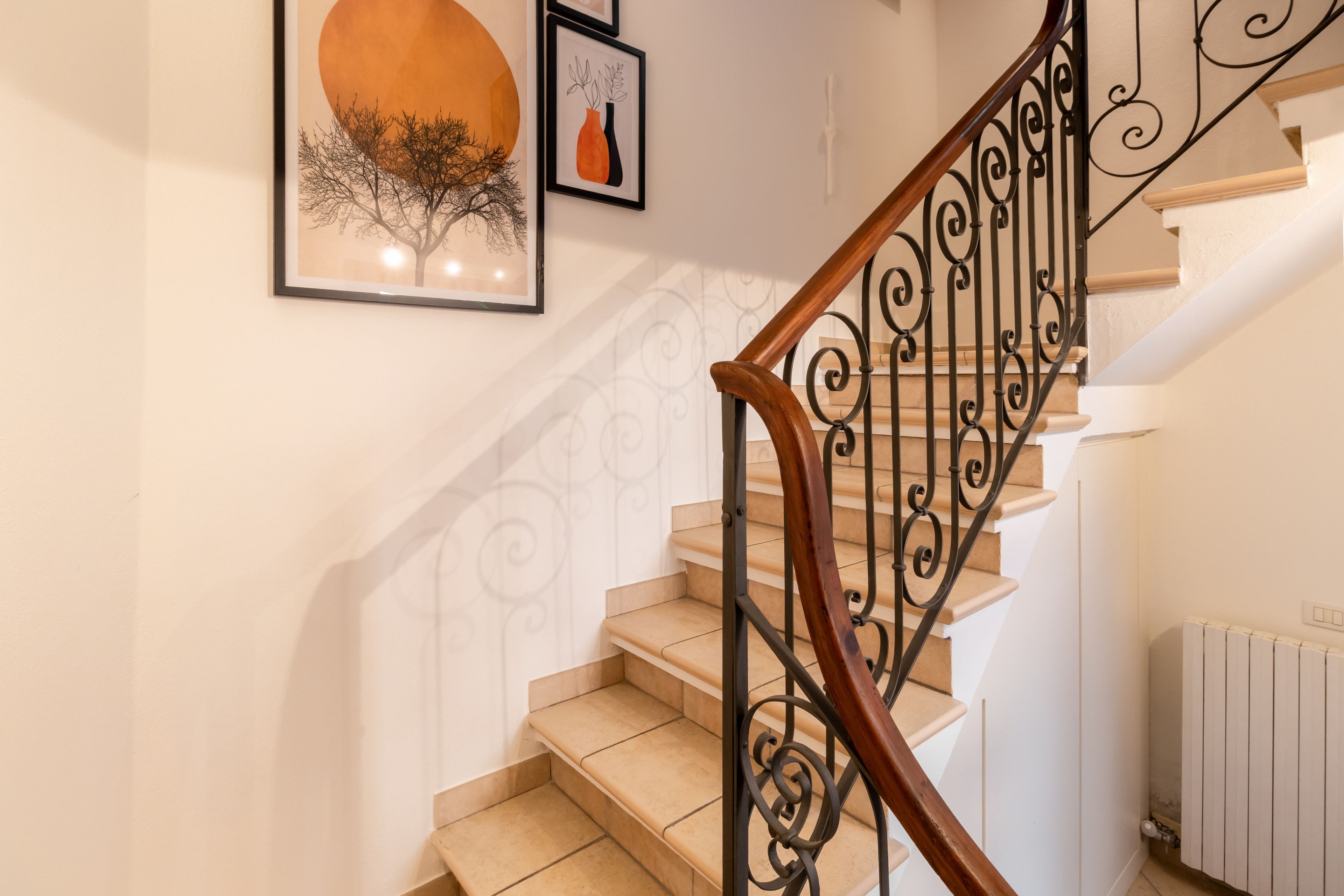 Eine Treppe mit hölzernem Geländer und schwarzen Metallspindeln, die zu einer Zwischenebene mit einem Heizkörper führt.