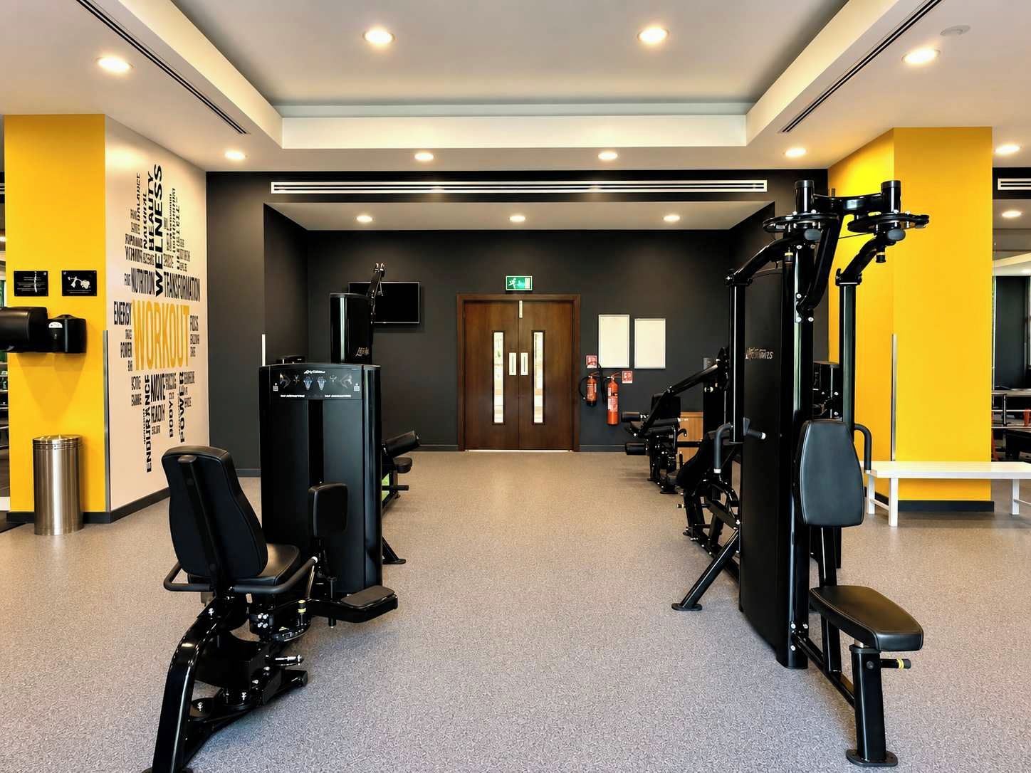 Ein Fitnessraum mit Trainingsgeräten, einer Wand mit motivierenden Sprüchen und einem Feuerlöscher.