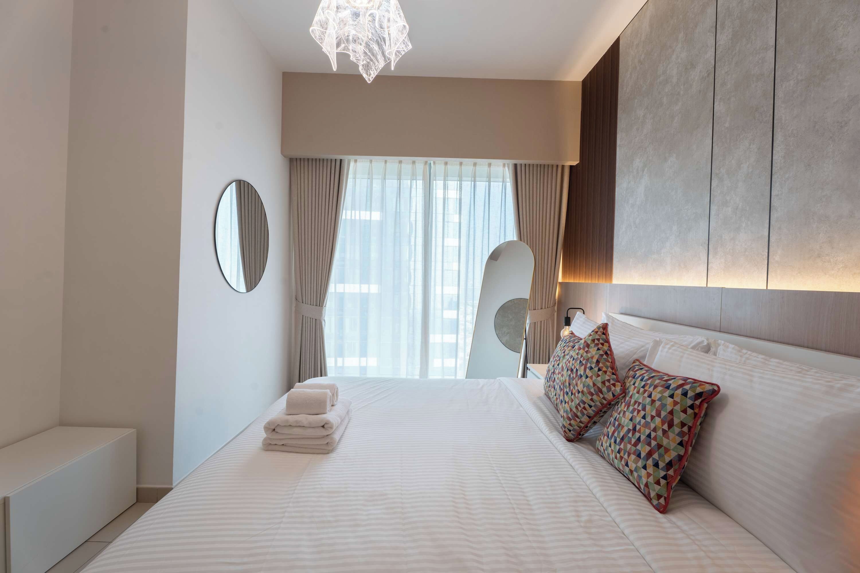 Ein modernes Hotelzimmer mit einem großen Bett, einem Nachttisch, einem Spiegel und Blick auf die Stadt durch das Fenster.