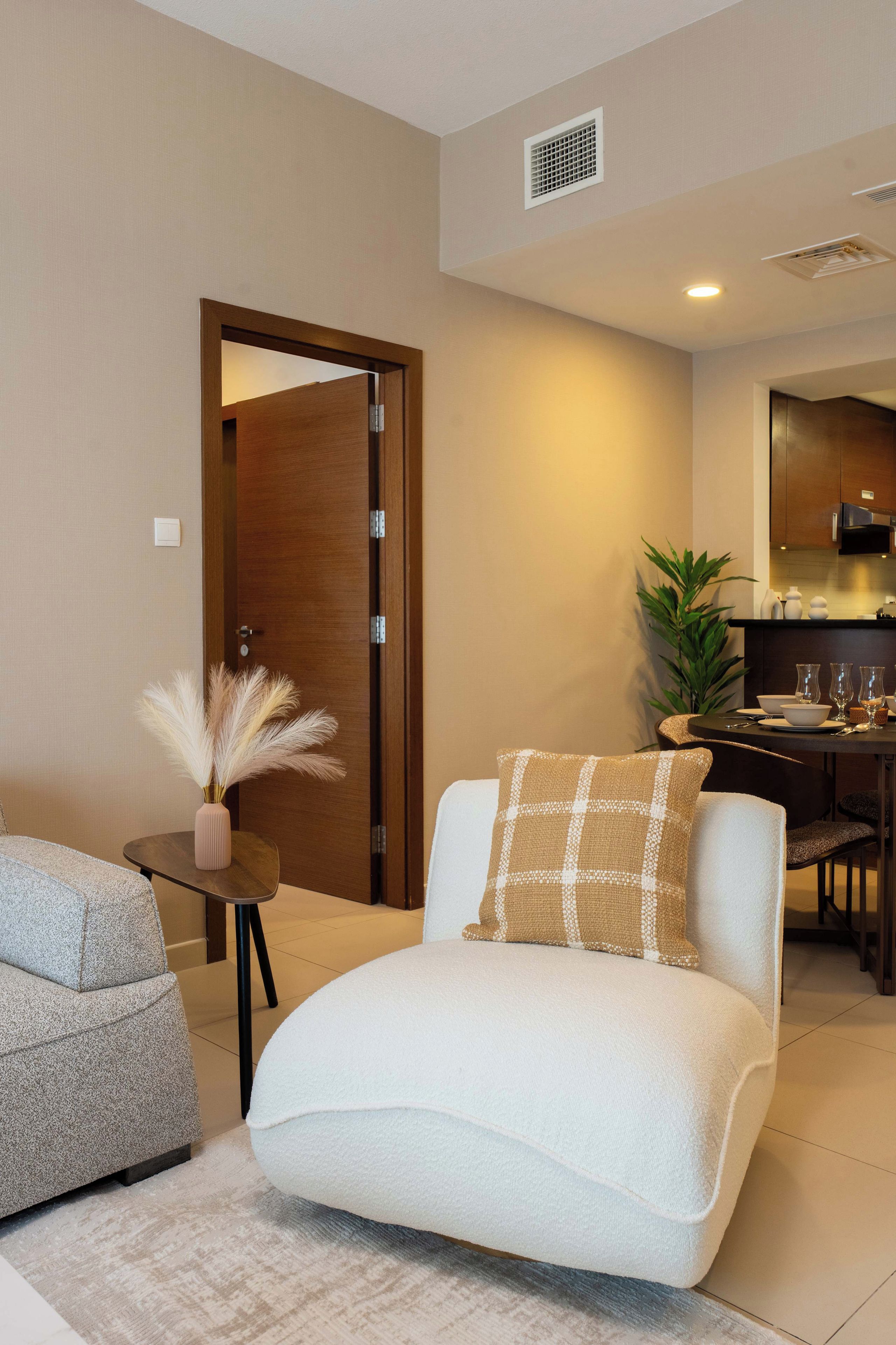 A modern living room with a sofa, a small table with a vase, and a dining area with chairs and a plant.