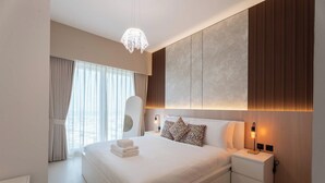 A modern hotel bedroom with a large bed, a bedside table, a nightstand, a hanging light fixture, and a view of the city through the window. - Vanilla Homes Premium 1BR in Gate Tower (Abu Dhabi)