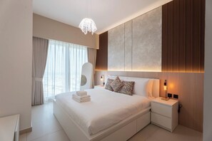 Un dormitorio de hotel moderno con una cama grande, una mesita de noche, una lámpara colgante y vistas de la ciudad a través de la ventana.