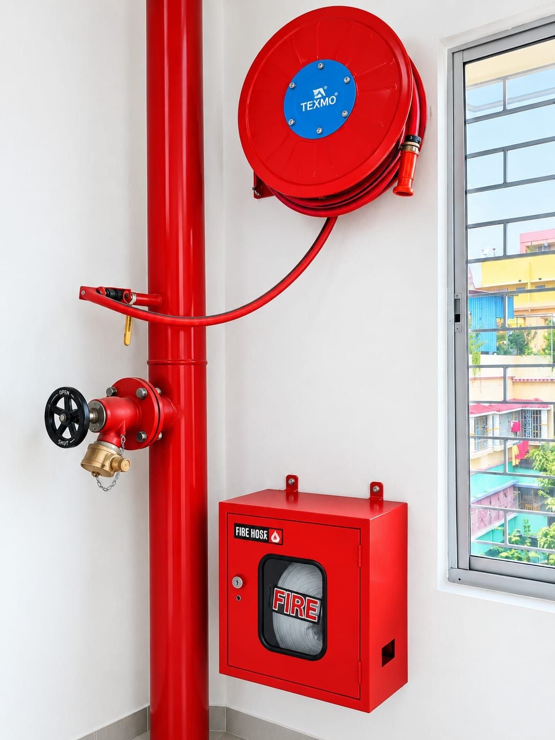 Un carretel rojo para manguera contra incendios montado en una pared, una llave para manguera y un armario rojo para manguera con un símbolo de fuego.