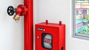 A red fire hose reel mounted on a wall, a fire hose valve, and a red fire hose cabinet with a fire symbol. - Hotel Maharaja Galaxy (Kolkata)