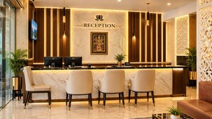 A reception area with a marble counter, four chairs, a chandelier, and a framed artwork above the counter. - Hotel Maharaja Galaxy (Kolkata)