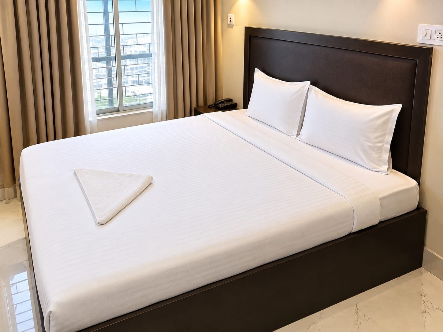 Una habitación de hotel con una cama grande, teléfono en la mesita de noche y una ventana con cortinas.