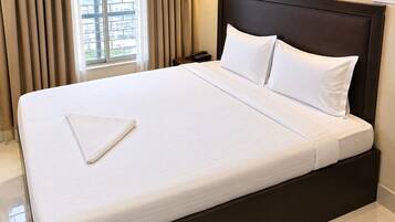 Una habitación de hotel con una cama grande, teléfono en la mesita de noche y una ventana con cortinas.