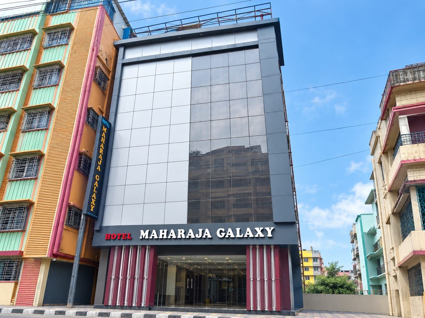 A modern hotel with a glass facade and a prominent sign reading 'MAHARAJI GALAXY HOTEL'.