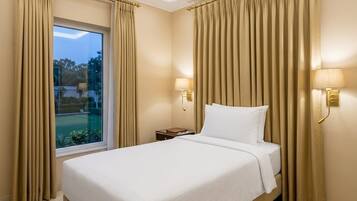 Habitación de hotel con una cama grande, cortinas, una mesita de noche, una lámpara y vistas al exterior.