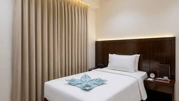 Una habitación de hotel con cama, cortinas, mesita de noche y mesilla auxiliar.