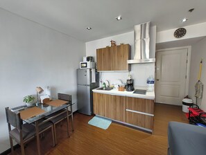 A compact kitchen with a refrigerator, microwave, and wooden cabinets. - A Cozy Unit with Hotel-Like Luxury Amenities & Near Mall (Makati City)