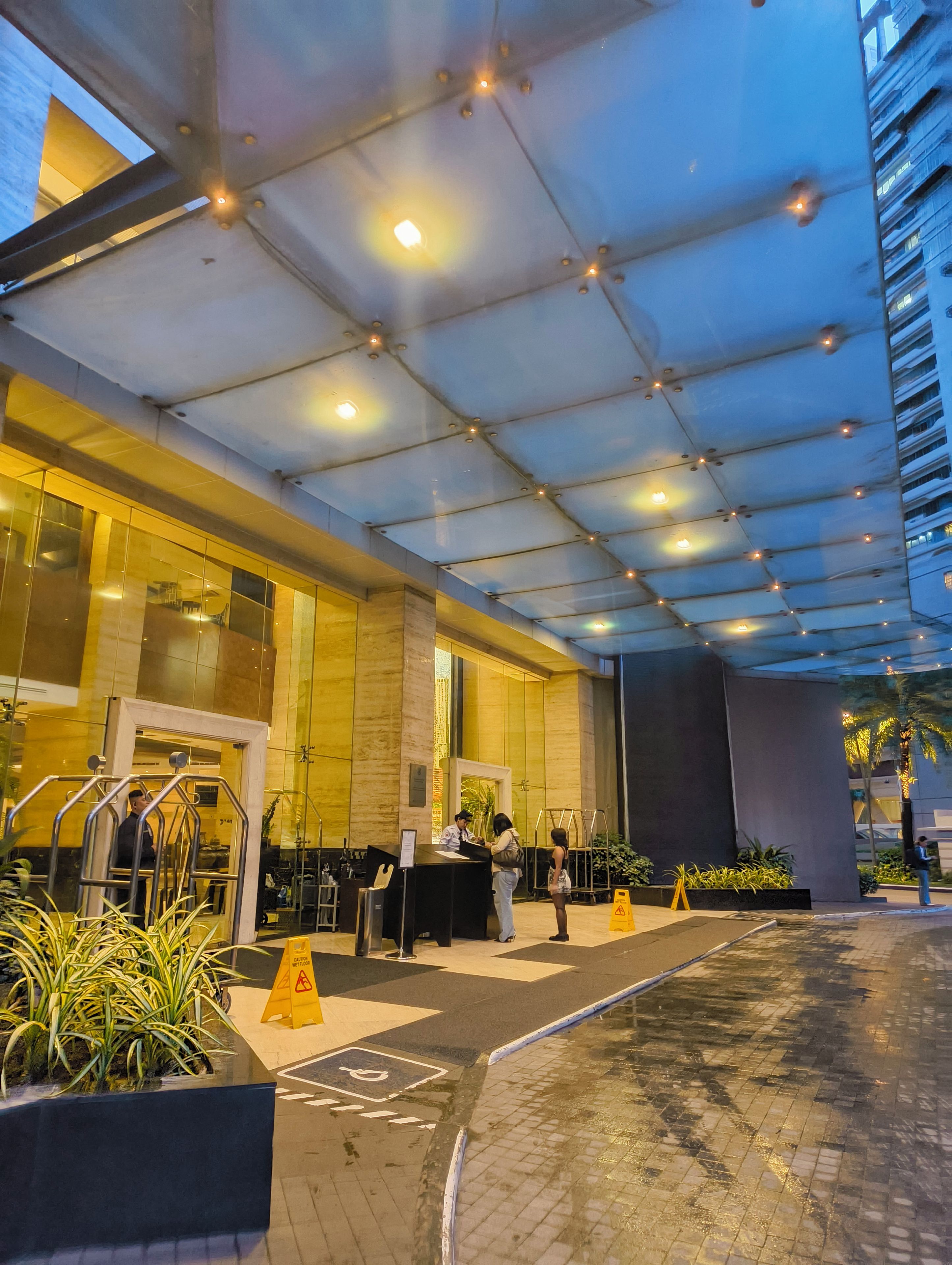 A hotel entrance with a reception desk, a glass door, and a covered walkway.