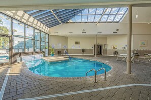 An indoor swimming pool with a glass ceiling, tiled floor, and poolside chairs. - A143 at The Myrtle Beach Resort (Myrtle Beach)