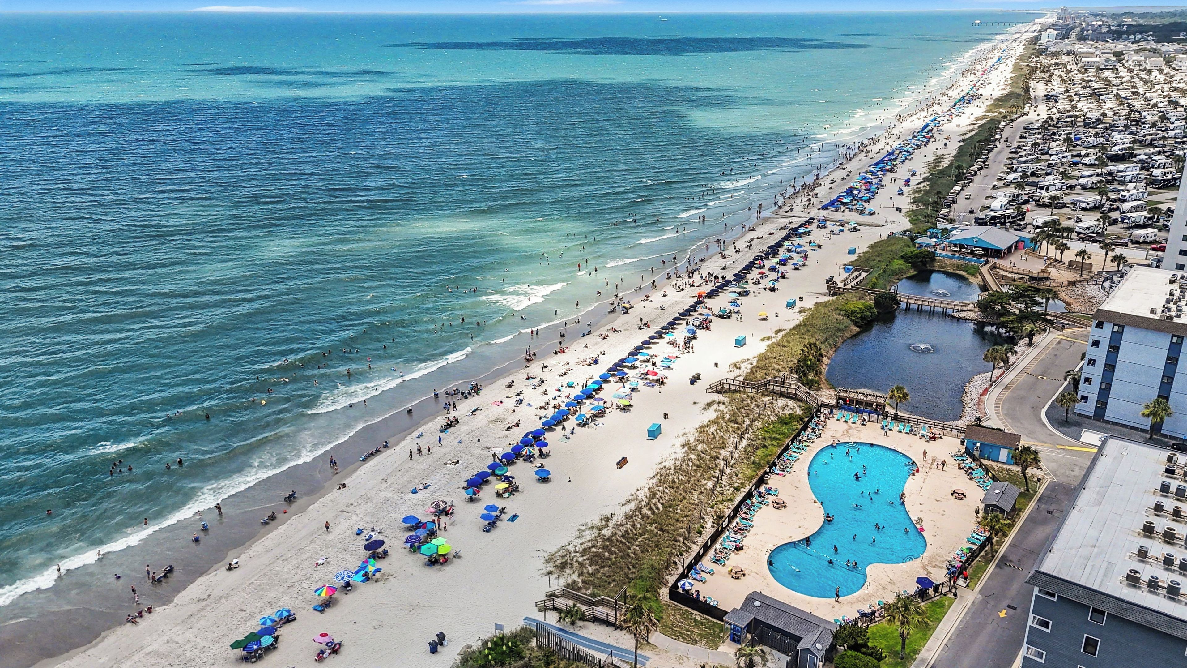 A beach with a swimming pool and beach umbrellas.