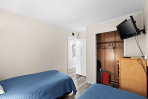 Quarto com duas camas, televisão fixada na parede e guarda-roupa de madeira.