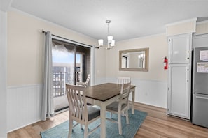 A dining area with a table and chairs, a ceiling light, a mirror, a refrigerator, and a sliding glass door leading to a balcony. - A540 at  The Myrtle Beach Resort (Surfside Beach)