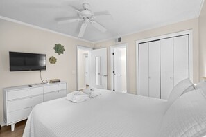 Une chambre d’hôtel avec un lit, une télévision, une commode et un ventilateur de plafond.