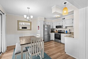 A modern kitchen with white cabinetry, stainless steel appliances, a dining area with a wooden table and chairs, and pendant lighting. - A540 at  The Myrtle Beach Resort (Surfside Beach)