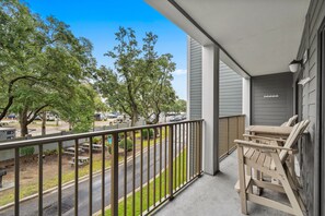 A balcony with a view of a parking lot and trees, a table with chairs, and a building with a number sign. - A245 Myrtle Beach Resort (Surfside Beach)