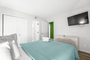 A bedroom with a bed, a dresser, a television mounted on the wall, and a door leading to another room. - A129 at the Myrtle Beach Resort (Myrtle Beach)
