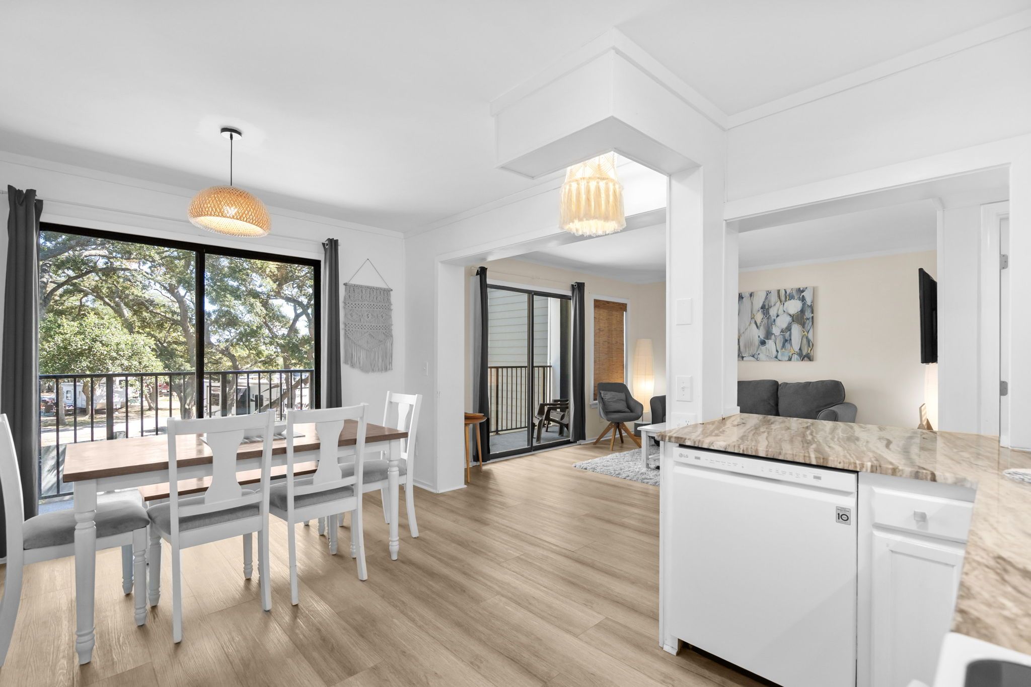 A modern kitchen with white cabinetry, a marble countertop, and a dining area with a wooden table and white chairs.