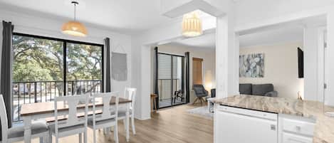 A modern kitchen with white cabinetry, a marble countertop, and a dining area with a wooden table and white chairs.