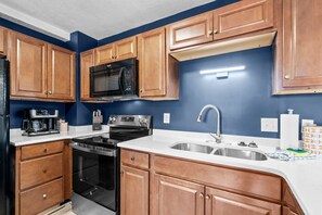 A kitchen with wooden cabinets, a microwave, a stove, and a sink. - B126 at The Myrtle Beach Resort (Myrtle Beach)