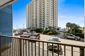 A high-rise building with multiple balconies, a parking lot with various vehicles, and a clear blue sky. - B126 at The Myrtle Beach Resort (Myrtle Beach)