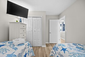 A bedroom with two beds, a dresser, a TV, and a door leading to another room. - B126 at The Myrtle Beach Resort (Myrtle Beach)