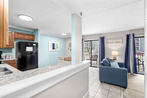 A modern kitchen with a black refrigerator, a white countertop, and wooden cabinets. - B141 at The Myrtle Beach Resort (Myrtle Beach)