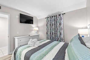A bedroom with a bed, a TV mounted on the wall, a bedside table with a lamp, and a window with patterned curtains. - B141 at The Myrtle Beach Resort (Myrtle Beach)