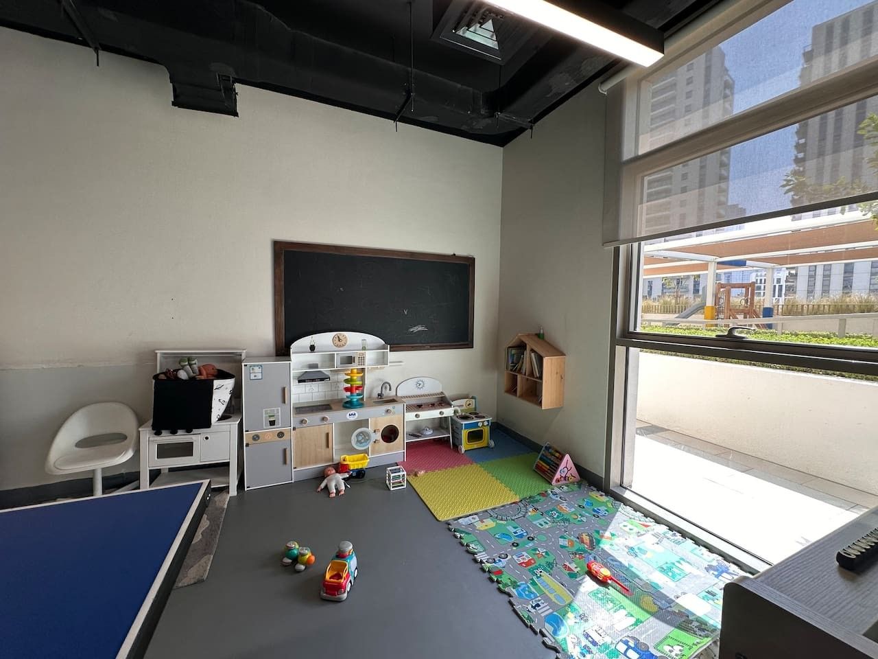 Een kinderspeelkamer met een blauwe tafel, speelmatten, speelgoed en een schoolbord.