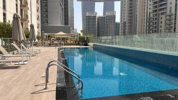 A swimming pool with a glass barrier, lounge chairs, and a view of tall buildings in the background.