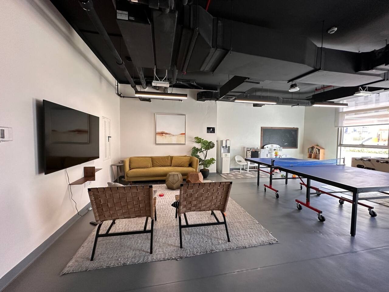 Een moderne kantoorruimte met een bank, twee stoelen, een tafeltennistafel en een flatscreen-televisie.