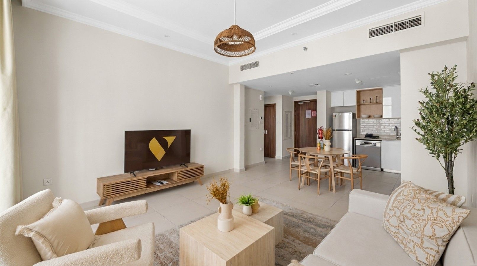 Een moderne woonkamer met een flatscreen televisie, een eethoek met een houten tafel en stoelen, en een keuken op de achtergrond.