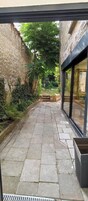 Un estrecho sendero al aire libre con pavimento de piedra que conduce a un edificio con amplios ventanales.
