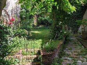 Um jardim com muro de tijolos, caminho de pedra e diversas plantas.