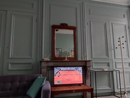 Una sala de estar con una televisión sobre un mueble bajo, un sofá, una chimenea y un espejo en la pared.