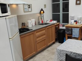 Cocina compacta con microondas, estufa, pileta y un pequeño comedor con mesa y sillas.