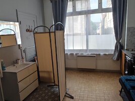 Una habitación pequeña y luminosa con baño, ventana con cortinas, radiador y lavabo.